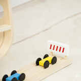 Toy cars on a wooden track with a small flag on a light wooden floor.