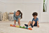Two children playing with a set of colorful wooden toy cars on a light wood floor.