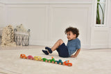 Child playing with colorful wooden toy cars on a light wood floor.