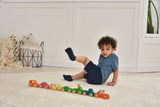 Child playing with colorful wooden toy cars on a light wood floor.