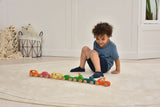 Child playing with colorful wooden toy cars on a light wood floor.