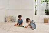 Two children playing with toys on a rug in a bright room with large windows.
