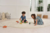 Two children playing with toy cars on a large white rug in a bright room.
