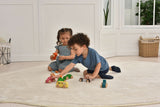 Two children playing with toy cars on a light-colored rug in a room with white walls and a window.