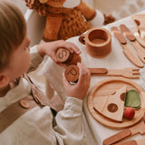 Child playing with wooden toys including a pepper grinder, plate with pizza slices, and utensils.